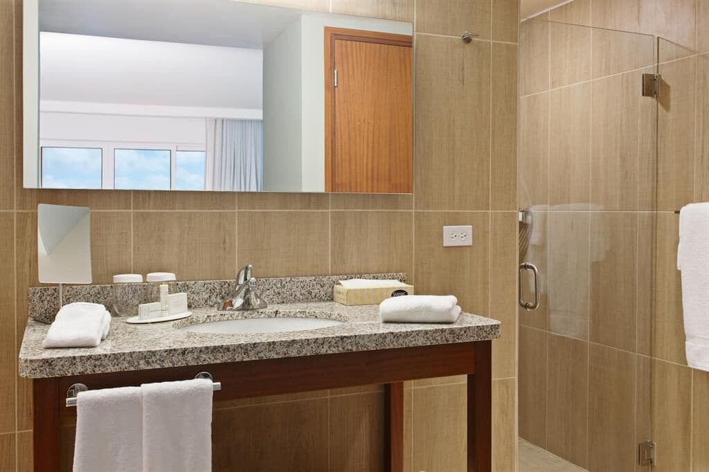 A modern bathroom with a granite countertop, a sink, a mirror, and a shower area.