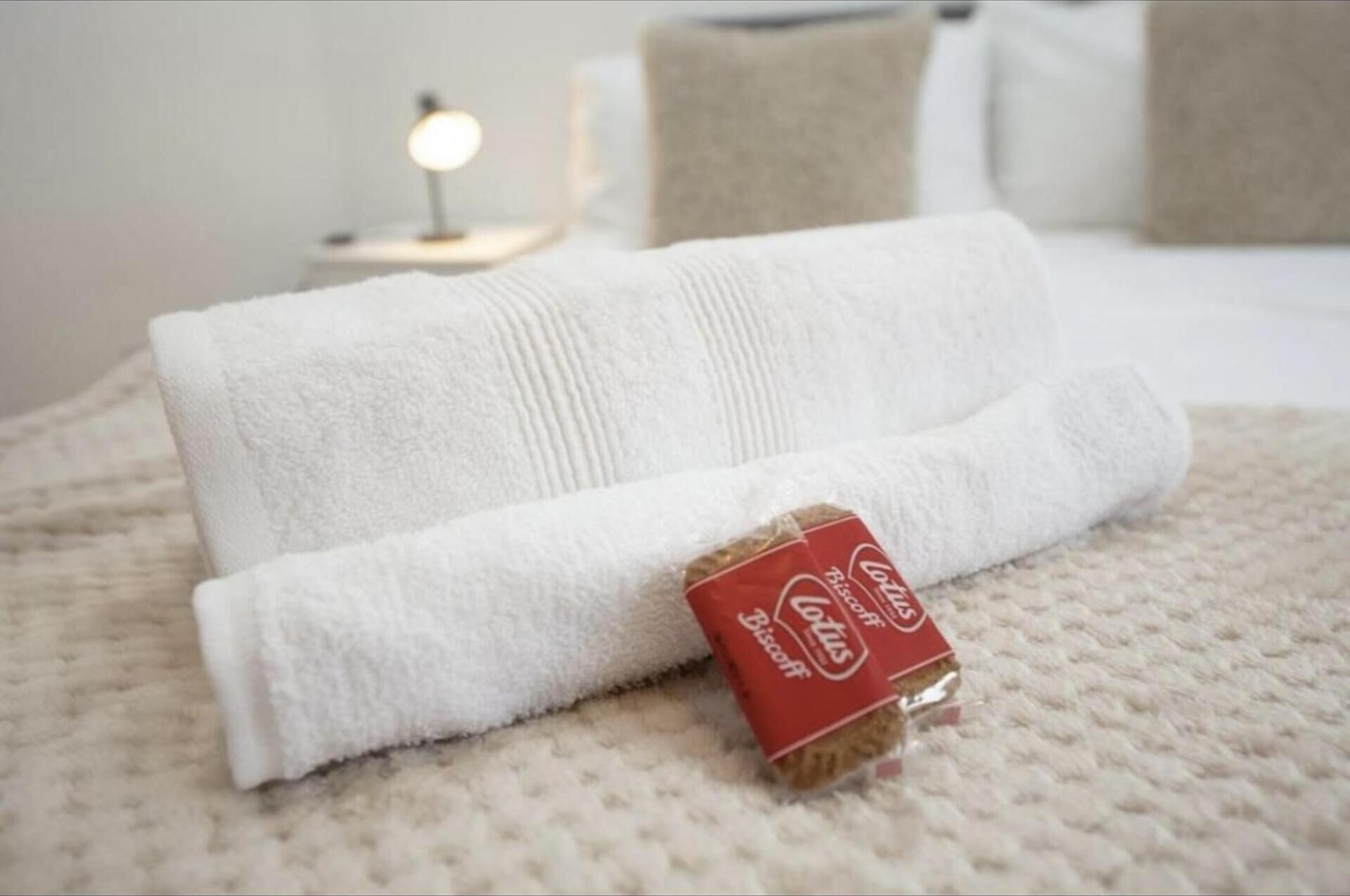 A neatly folded white towel and a small red packet on a textured beige bedspread.