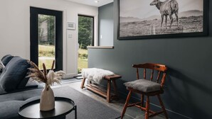 Ett modernt vardagsrum med en grå soffa, en trästol, ett litet bord med en vas och ett inramat fotografi av vilda djur på väggen.