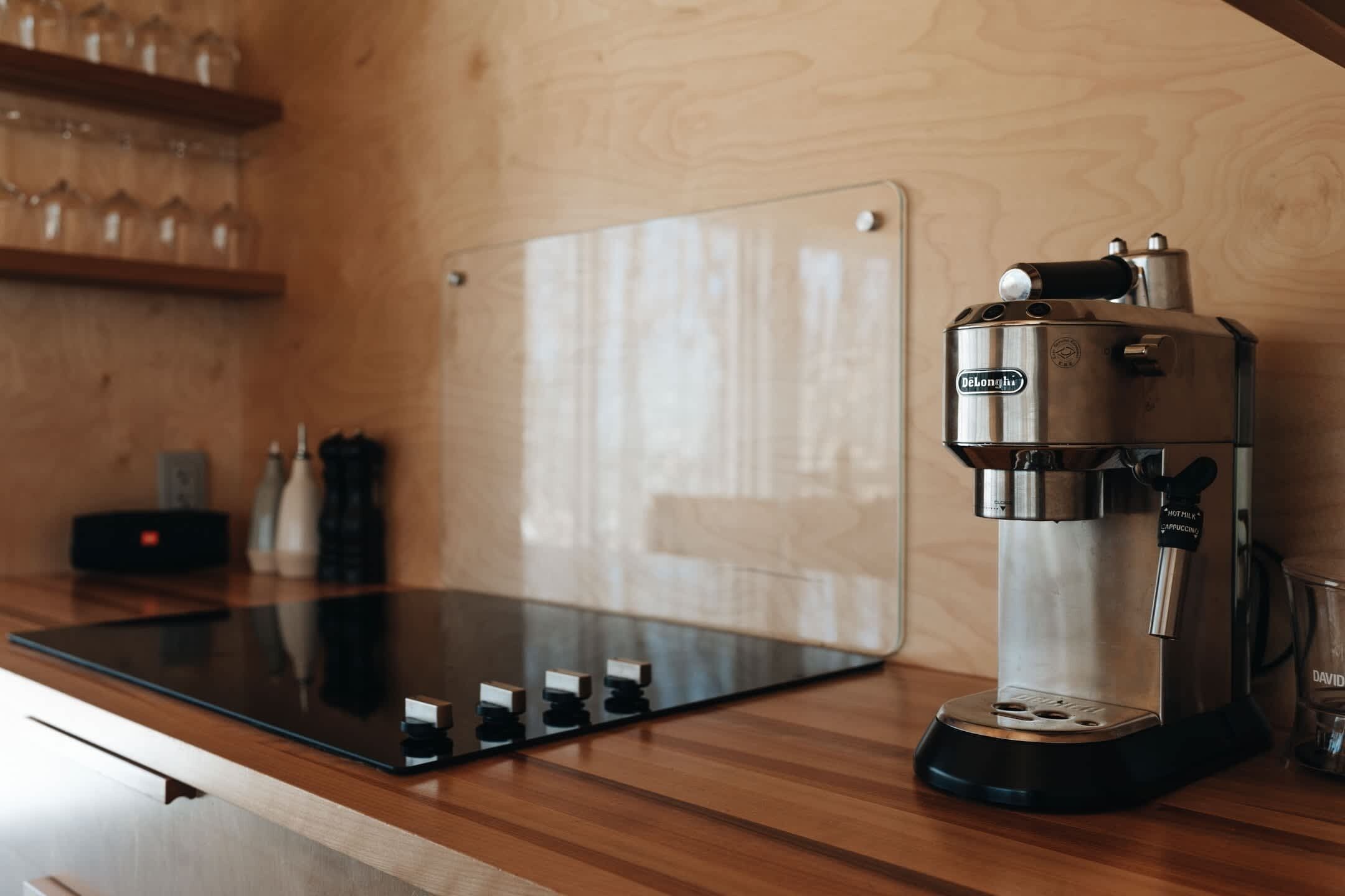 Une machine à café est posée sur un comptoir en bois, avec un panneau en verre et quelques petits objets sur le côté gauche.