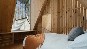Dormitorio de cabaña de madera con cama, ventana y vista al bosque.