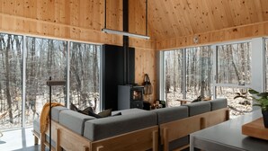 Interior de una cabaña moderna con un gran techo de madera, un espacio de estar acogedor con sofá y banco, una mesa y una chimenea.