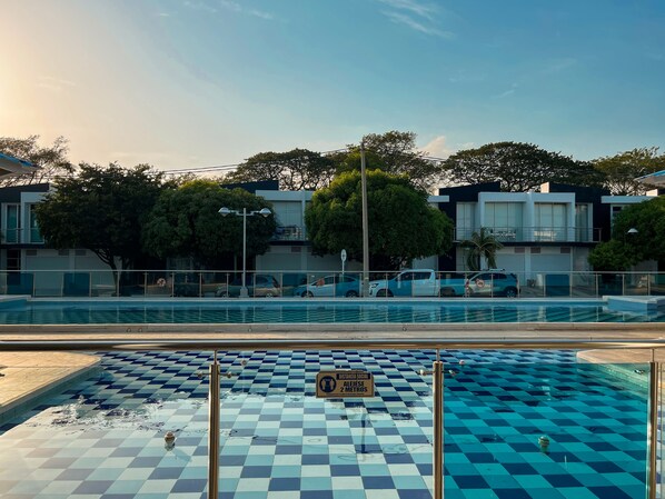 A swimming pool with a checkered pattern, surrounded by a fence, with a sign indicating a social distancing measure of 2 meters.