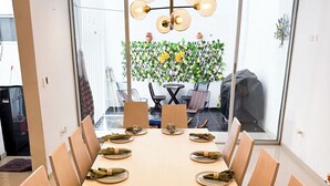 Ein Essbereich mit einem langen Tisch, gedeckt für eine Mahlzeit, umgeben von Stühlen und einer dekorativen Leuchte darüber.