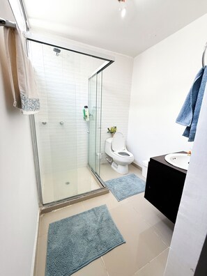 A modern bathroom with a glass shower enclosure, a toilet, and a sink with a black vanity.