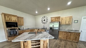 Une cuisine spacieuse dotée de meubles en bois, d’un réfrigérateur en acier inoxydable, d’un four encastré et d’un îlot central avec un plan de travail en marbre.