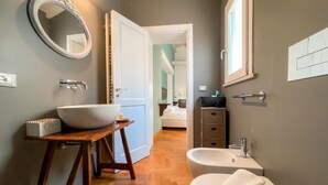 Un baño con un espejo redondo grande, un lavamanos pedestal, un bidé y un taburete de madera.
