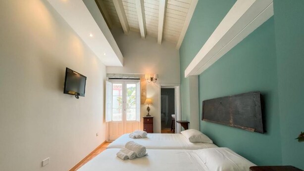 Habitación de hotel con dos camas, un televisor de pantalla plana, un ventanal grande y una puerta que da a un balcón.