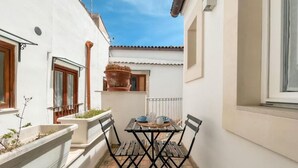 Un pequeño patio exterior con una mesa y sillas, rodeado de paredes blancas y plantas en macetas.