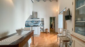 Un pasillo estrecho con una zona de cocina a la izquierda, que presenta un suelo tipo espiga, una mesa de madera y un banco blanco.