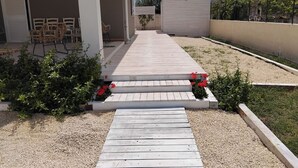 Un camino de madera que lleva a una zona de estar al aire libre cubierta con sillas y mesas.