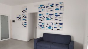 Una habitación con un sofá azul, paredes blancas y varias obras de arte con motivos de peces enmarcadas.