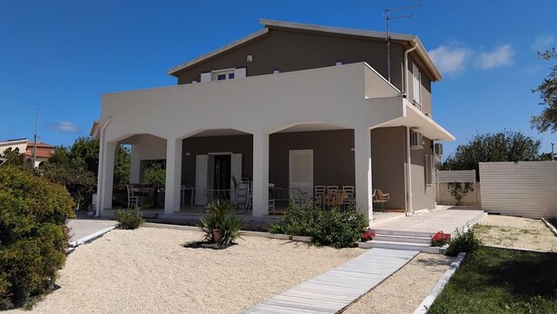 Una casa de dos pisos con un porche cubierto, un pequeño jardín y un camino de entrada de grava.