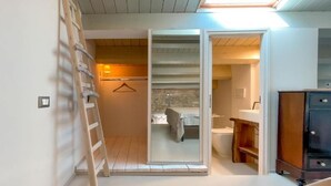 A compact room with a wooden ladder, a bed, a bathroom, and a cabinet.