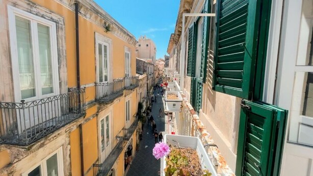 A narrow street flanked by buildings with balconies and shutters.