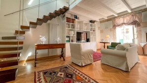 A spacious living area with a staircase, a bookshelf, a sofa, and a patterned rug.