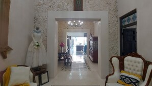 Uma sala de estar ampla com um candelabro, uma poltrona branca, um tapete estampado e vista para outro cômodo.