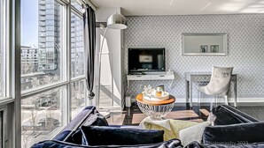 A modern living room with a large window, a flat-screen TV, a white console table, and a chair. - Cozy Condo near CN Tower - downtown (Toronto)