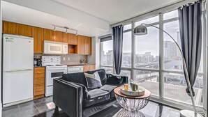 A modern apartment with a kitchen, a black leather sofa, a round coffee table, and a large window with curtains. - Cozy Condo near CN Tower - downtown (Toronto)