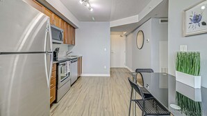 A modern kitchen with stainless steel appliances, wooden cabinets, and a dining area with a glass table and chairs. - Beautiful Condo Near Subway station (Toronto)