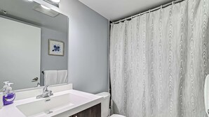 Une salle de bain avec un lavabo blanc, un miroir, des toilettes et un rideau de douche.