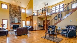 A spacious living room with a stone fireplace, leather sofas, a coffee table, and a staircase leading to an upper level. - Dog-Friendly 2BR Lodge, Pool by Big Cedar (Hollister)