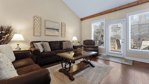 A living room with a brown leather sofa, a glass coffee table, and a wooden floor. There are two lamps on side tables, a painting on the wall, and a ceiling fan. - Dog-Friendly 2BR Lodge, Pool by Big Cedar (Hollister)
