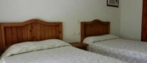 Una habitación con dos camas, cada una con cabecero de madera y una mesita de noche.
