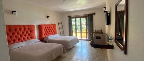 Habitación de hotel con dos camas, una mesita pequeña, una silla, una escalera y una ventana con cortinas.