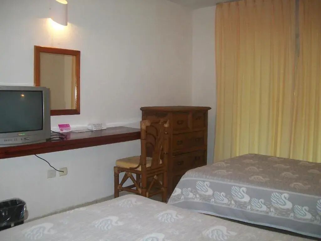 Une chambre d’hôtel comprenant un lit, une commode en bois, un bureau avec une télévision et un miroir.
