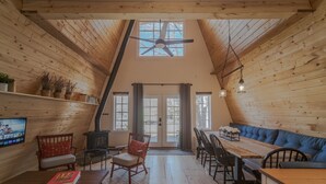 A cozy loft-style room with wooden walls and a sloped ceiling, featuring a dining table, chairs, a sofa, a fireplace, and a television. - The Cabin on Main St., A Quiet Getaway with whole family, History. Pet friendly. (Spring City)