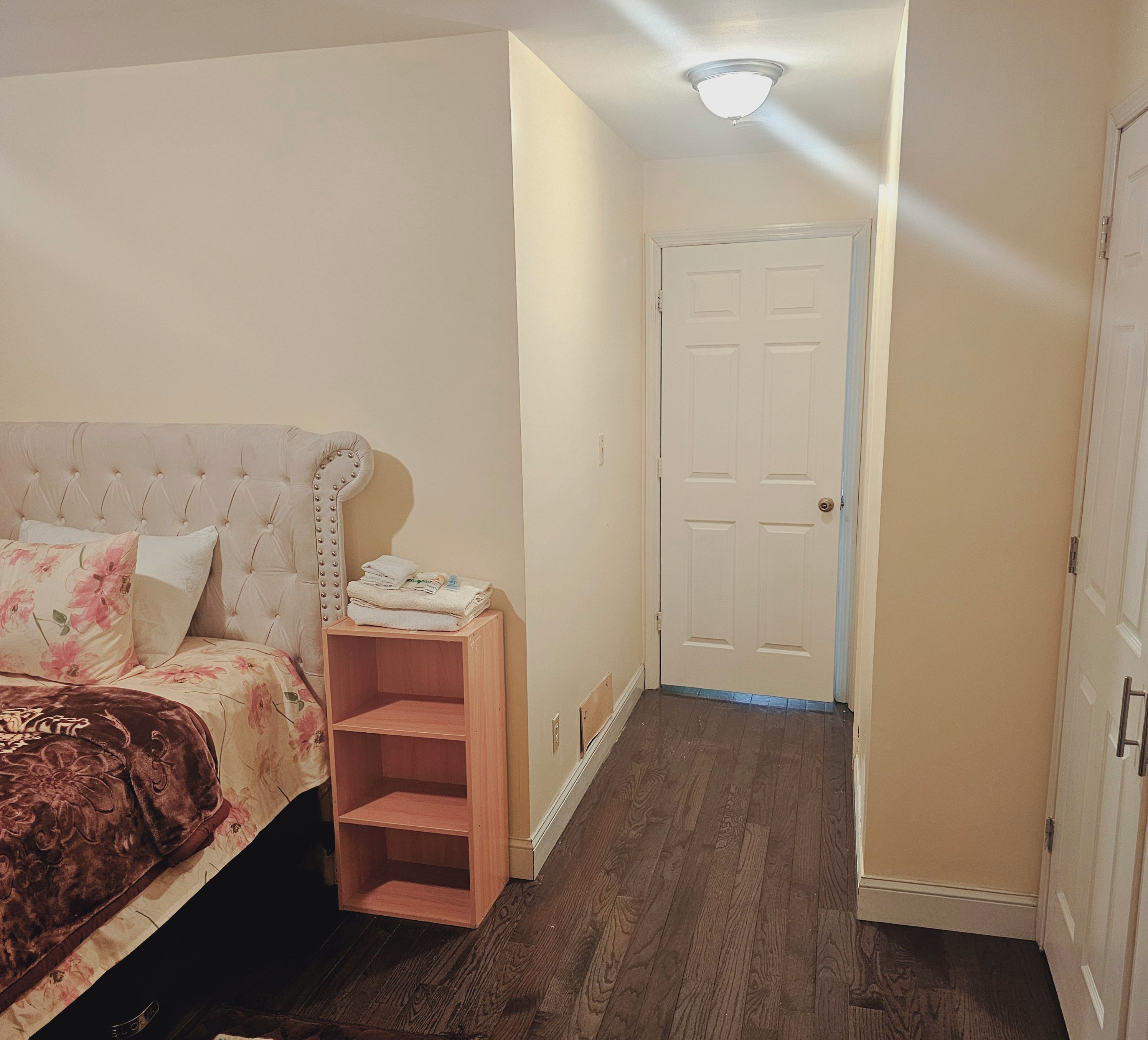 A bedroom with a bed, a wooden shelf, a door, and a hallway.