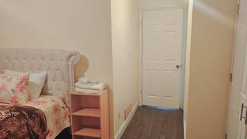 A bedroom with a bed, a wooden shelf, a door, and a hallway.
