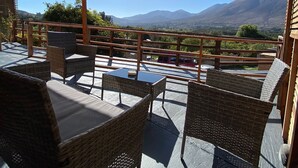 Eine Terrasse im Freien mit Korbmöbeln und einem Tisch, mit Blick auf eine gebirgige Landschaft.
