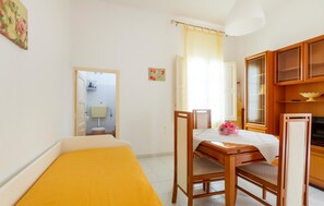 A small, well-lit room with a wooden table, two chairs, a bed with a yellow bedspread, a window with a curtain, and a cabinet with glass doors. - 1 bedroom gorgeous home in Taviano (Taviano)