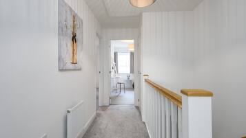 Un couloir avec un radiateur blanc, une main courante en bois et un luminaire au plafond.