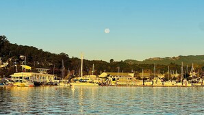 Un puerto deportivo con barcos amarrados, un edificio con balcón y una colina al fondo.