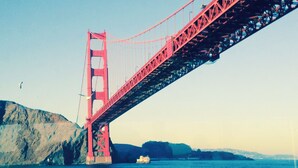 Un puente rojo ancho que cruza un cuerpo de agua, con montañas al fondo.