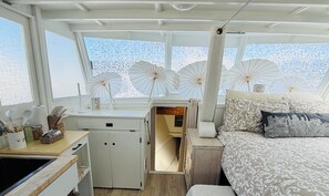 Ein gemütlicher Raum mit Bett, einer kleinen Küchenzeile und einem Fenster mit dekorativen Regenschirmen.