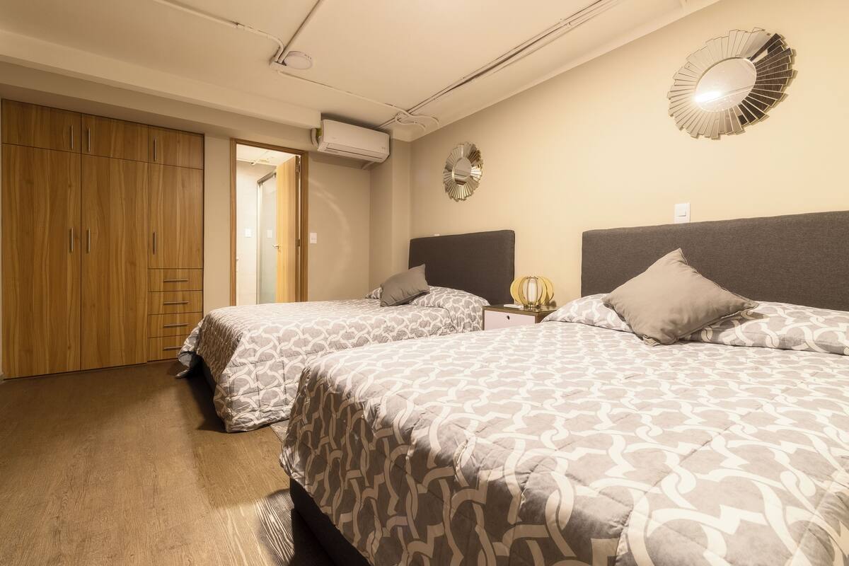 A bedroom with two beds, wooden wardrobe, and a wall-mounted mirror.
