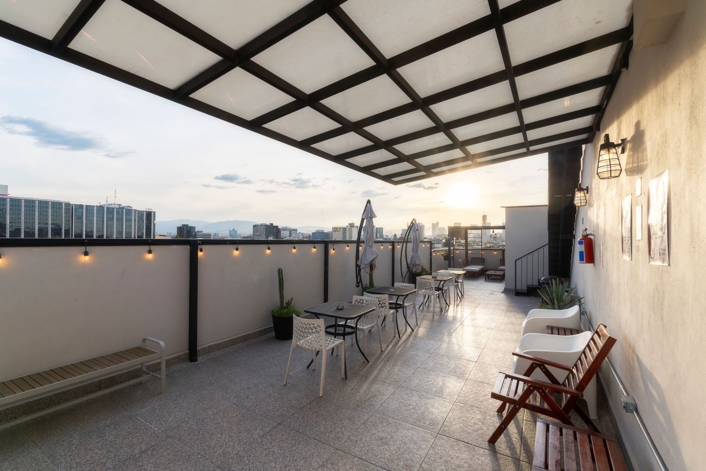 A rooftop terrace with tables and chairs, a bench, and a view of the cityscape.