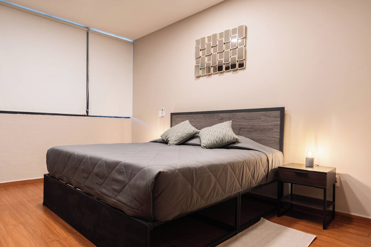 A modern bedroom with a bed, bedside table, and a wall-mounted light fixture.