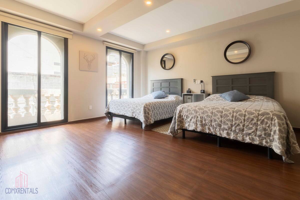 A bedroom with two beds, a large sliding glass door, a round mirror, and a small bedside table.