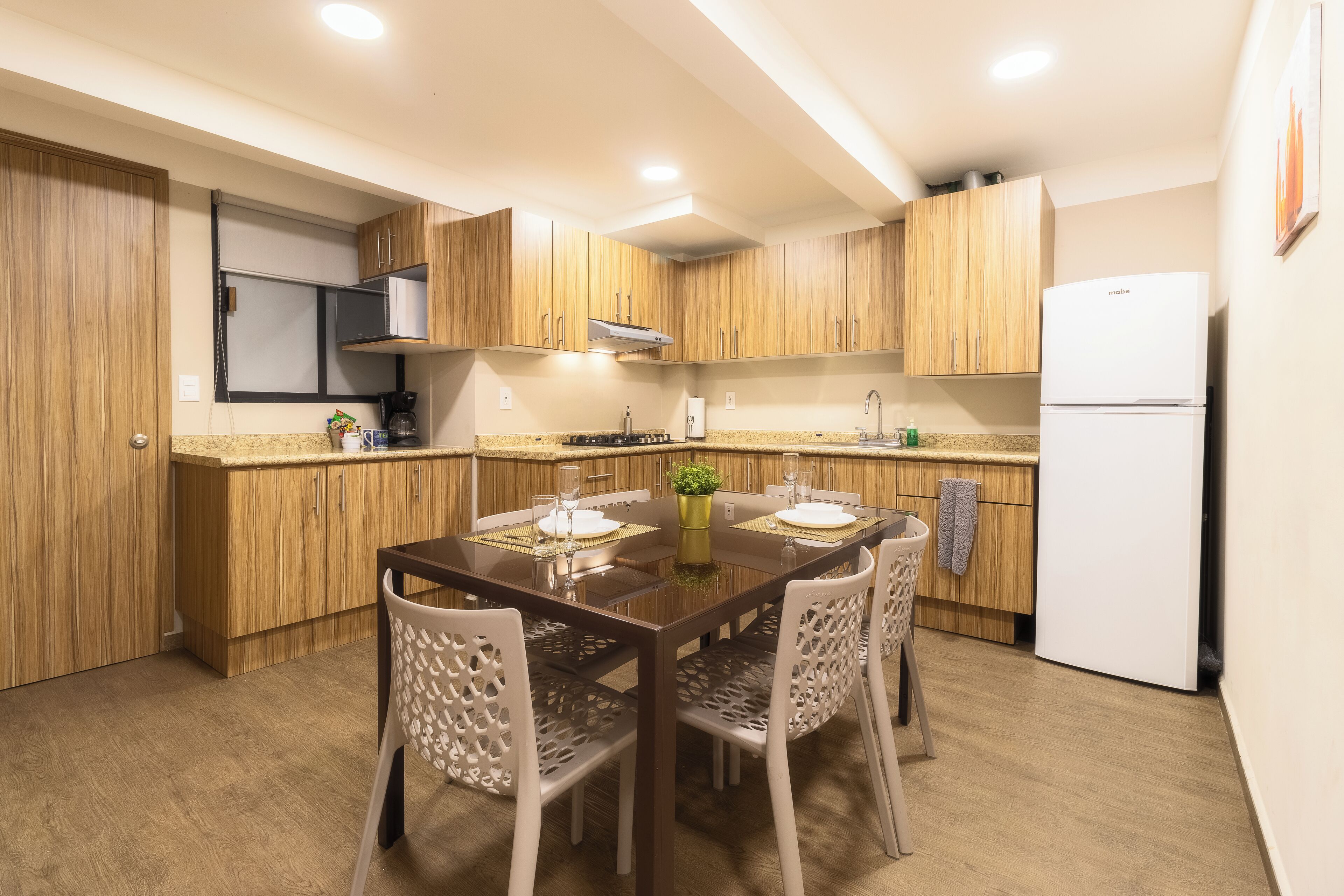 A compact kitchen with wooden cabinets, a white refrigerator, and a dining table set for four.