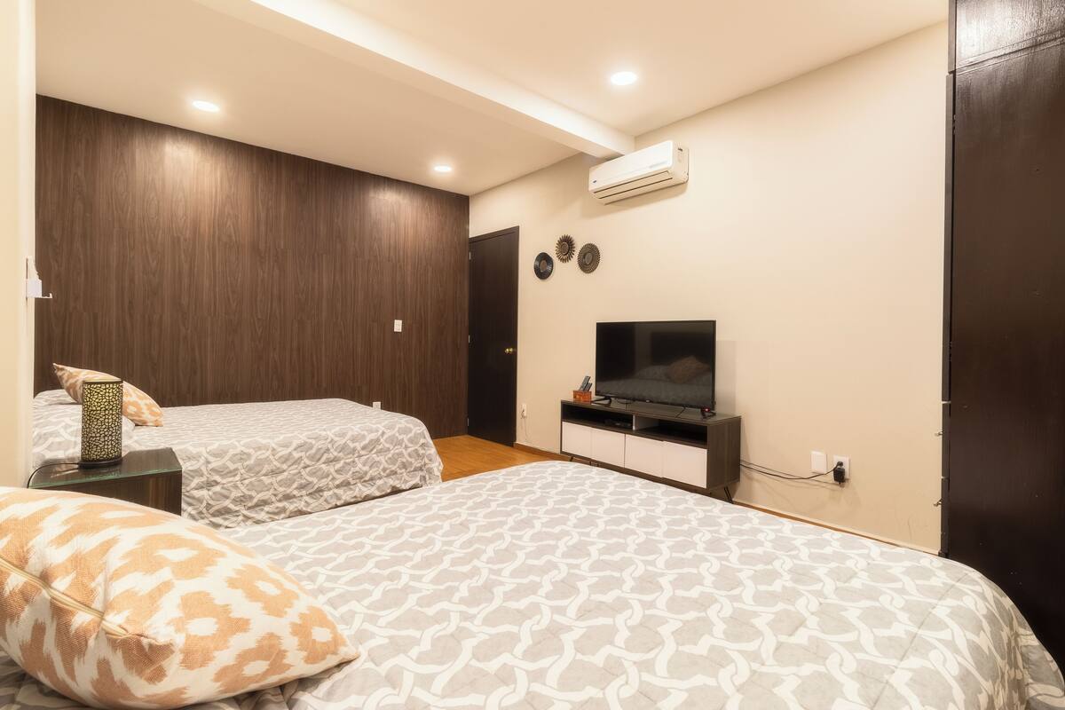 A bedroom with two beds, a TV, and an air conditioner.