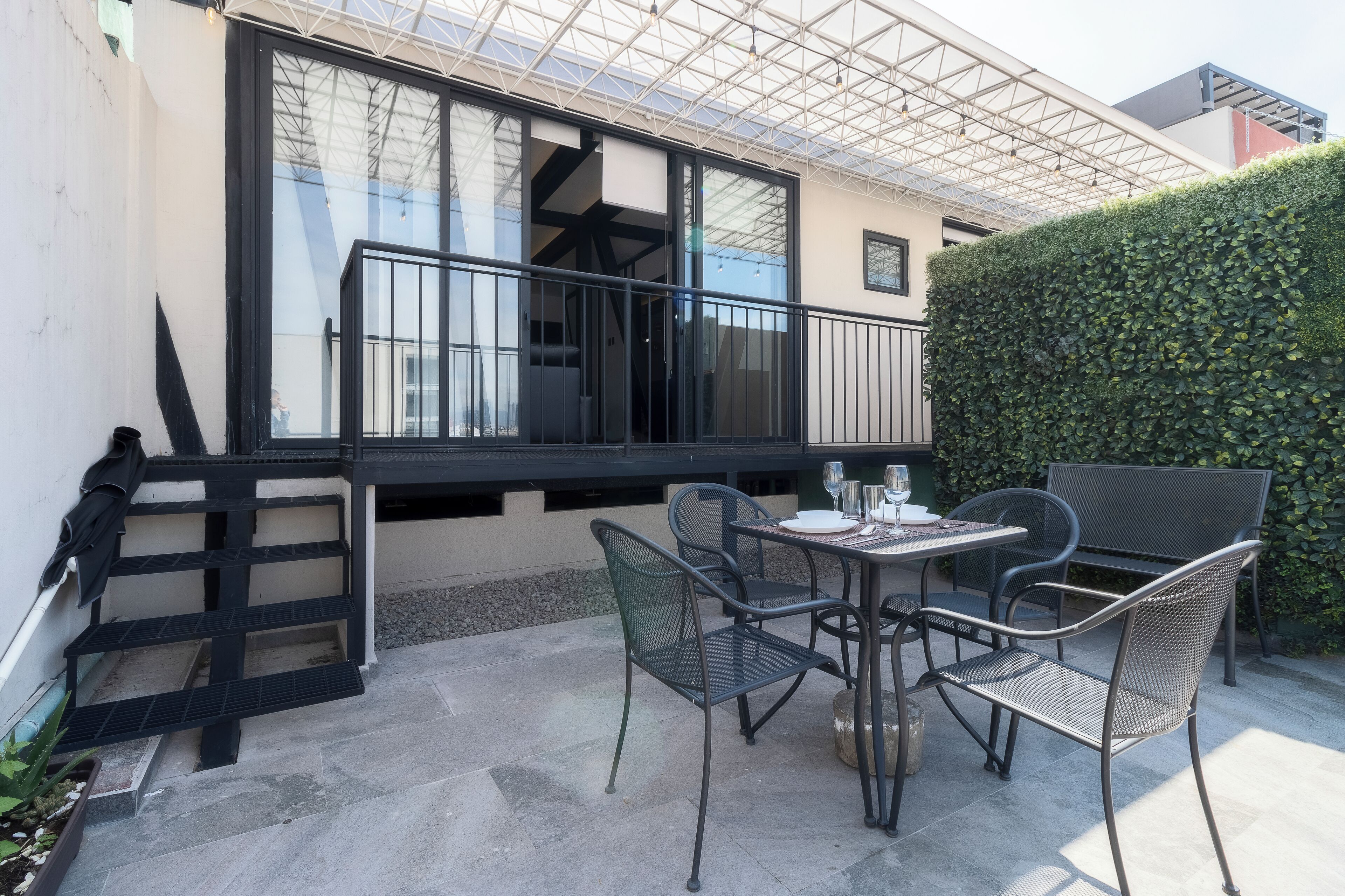 Un patio con una mesa y sillas, baranda negra y un seto.