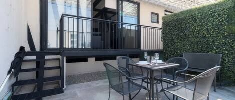 Un patio con una mesa y sillas, baranda negra y un seto.
