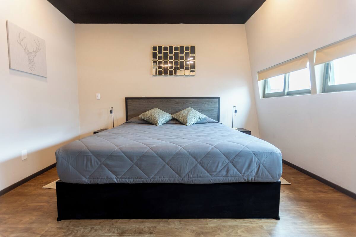 A bedroom with a bed, a headboard, a wall-mounted mirror, and a window with blinds.