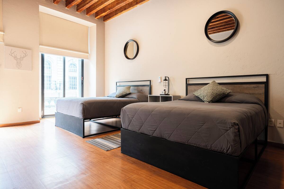 A bedroom with two beds, a large window, and a wooden ceiling.