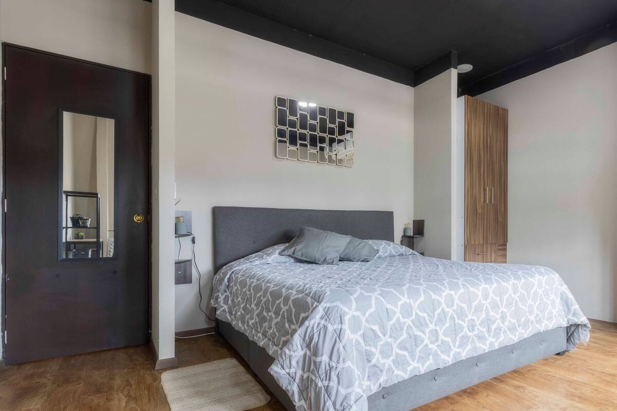 A bedroom with a bed, a wooden floor, a door, a wall-mounted shelf, and a wardrobe.